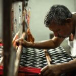 Weaver operating an industrial loom producing cotton and polyester cotton canvas fabric in India